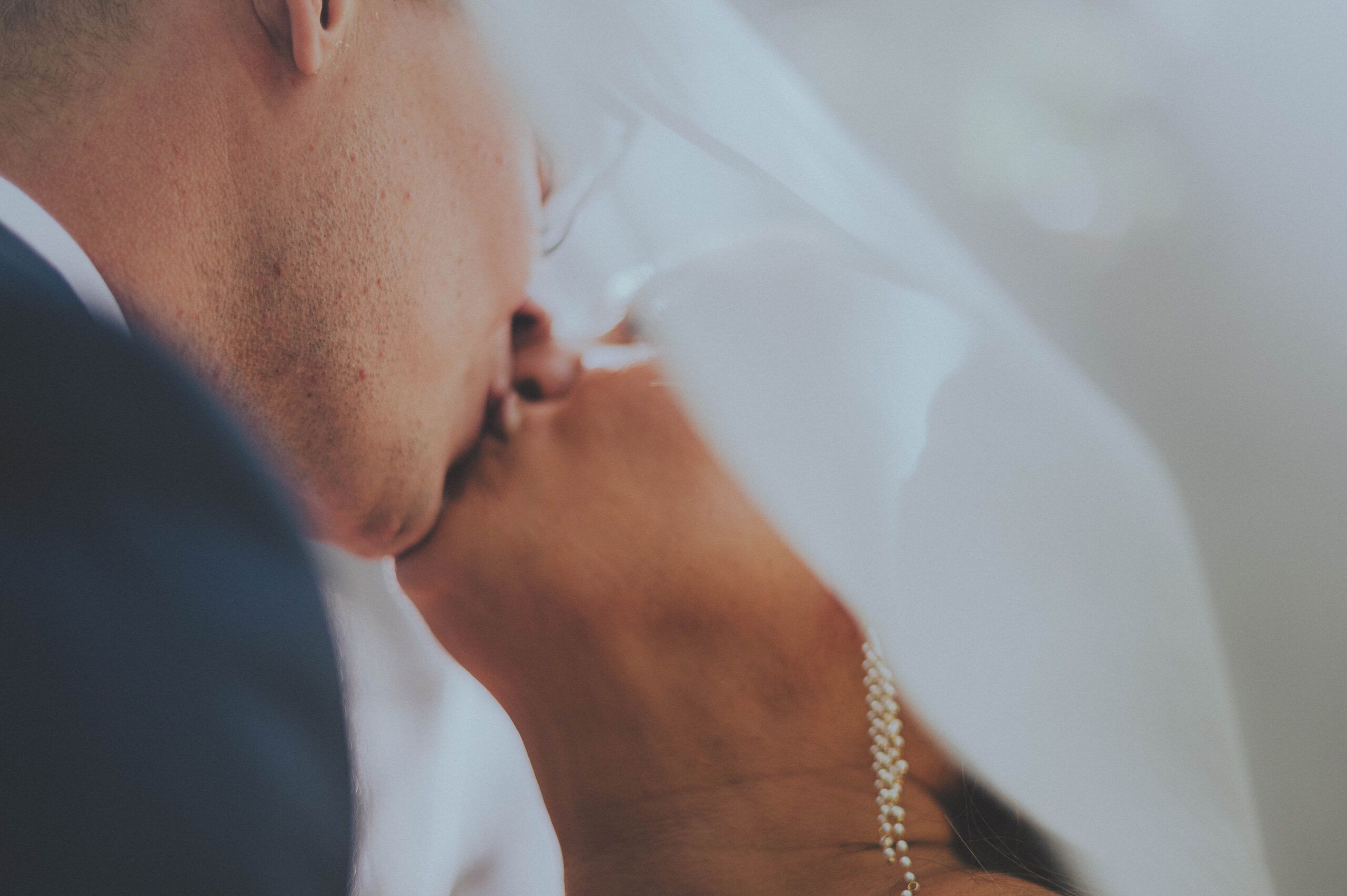 An intimate close-up of a kiss beneath a softly lit wedding veil.