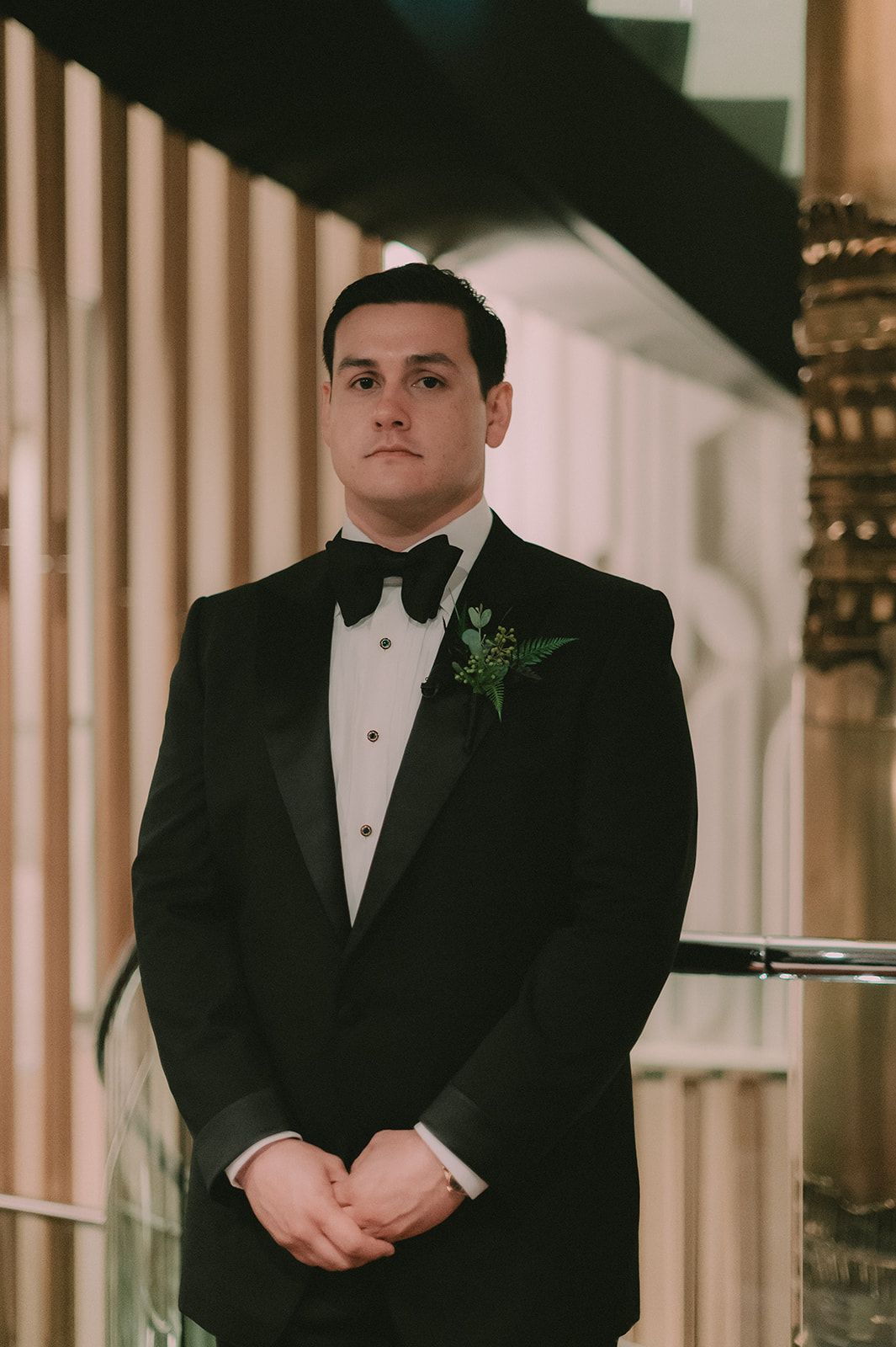 Charles stands in a black tuxedo beside the curved staircase at The Jay Hotel.