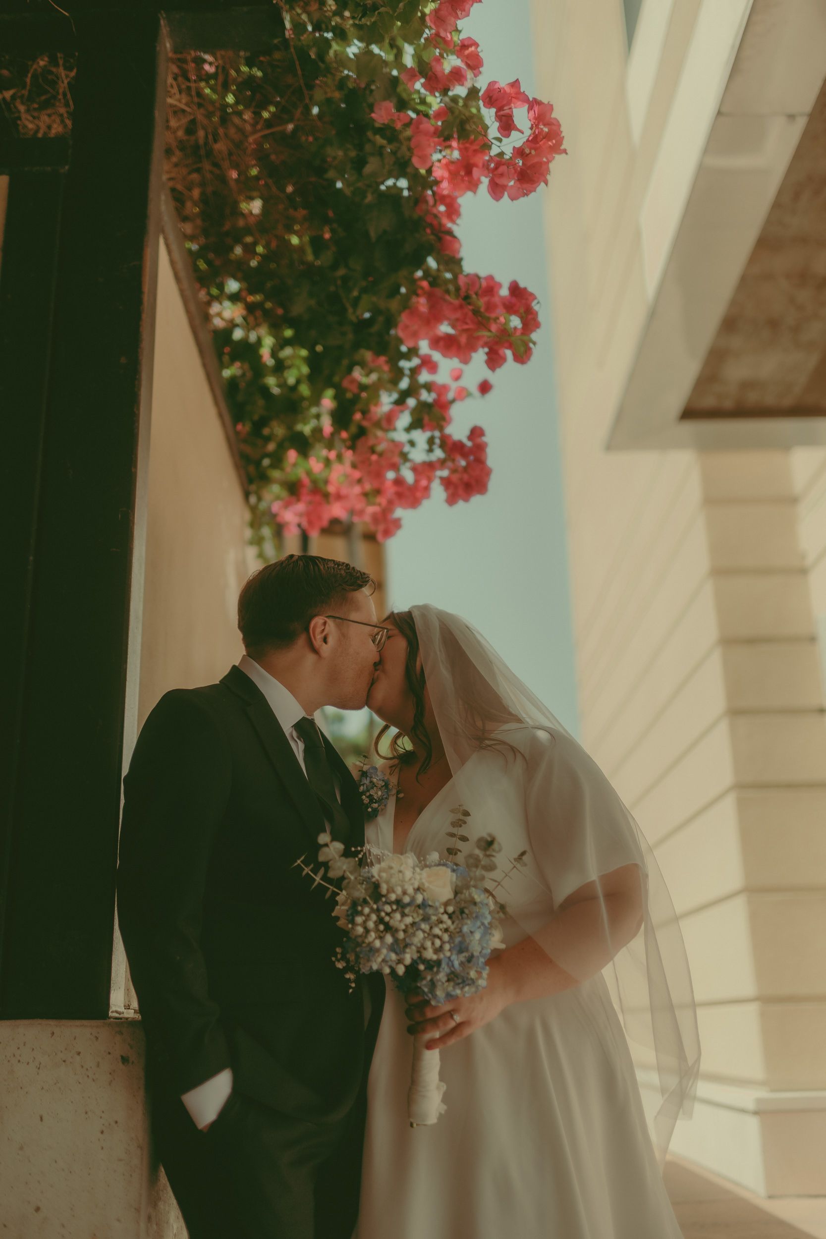 Tiffani and Braden kiss beside flowers and downtown architecture.