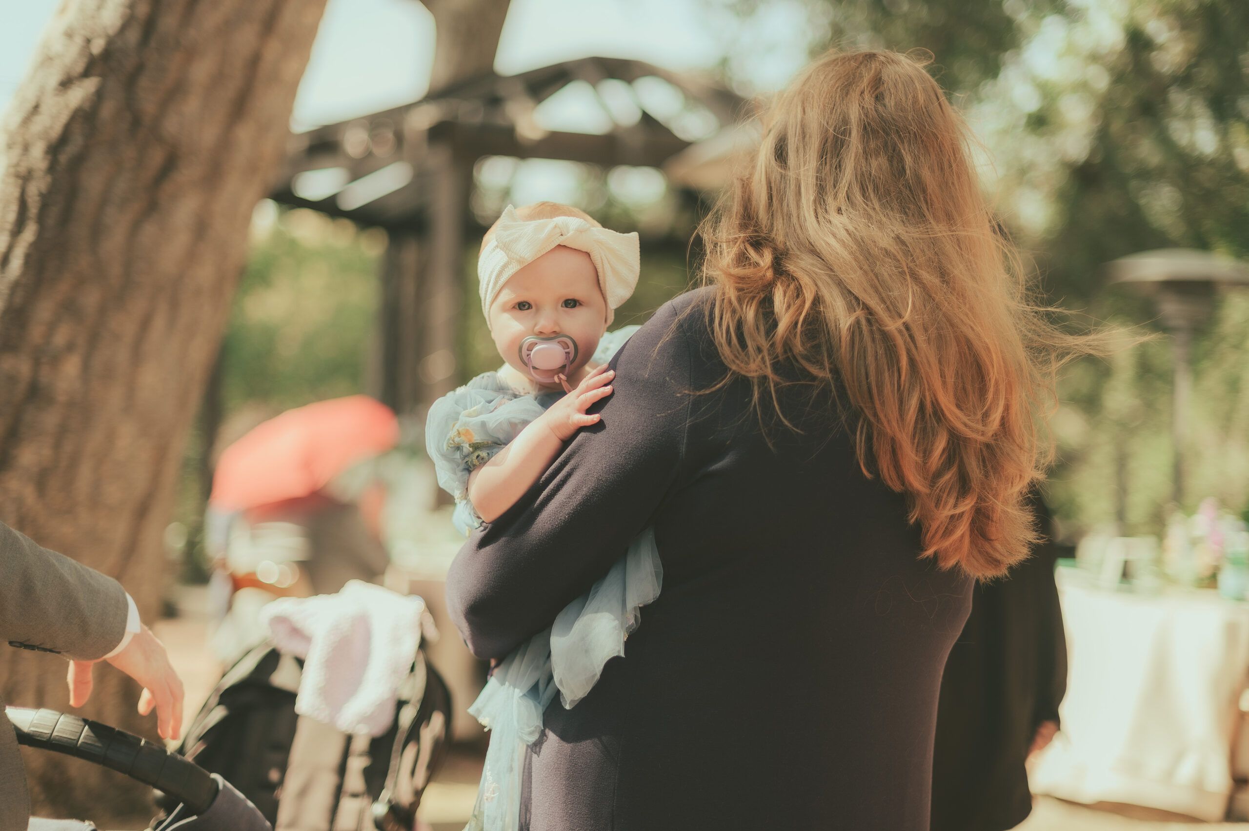 A baby looking over a guest’s shoulder at an outdoor celebration.
