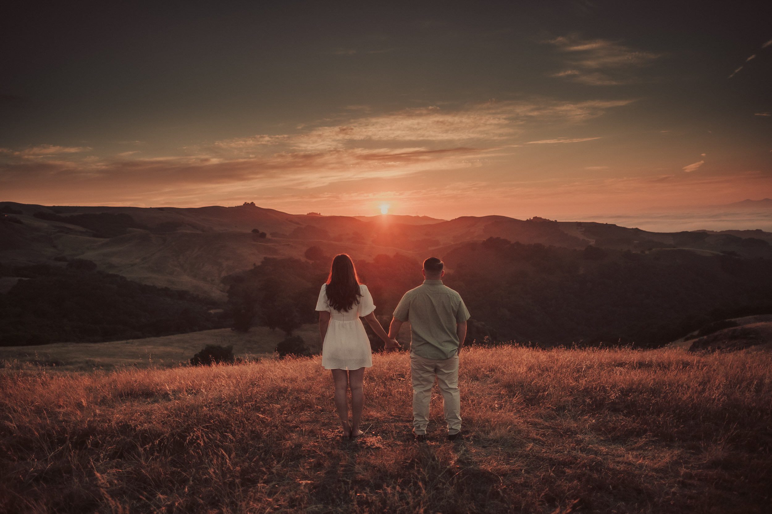 Lauren and Bennett holding hands as the sun sets over the rolling hills from Prefumo Canyon