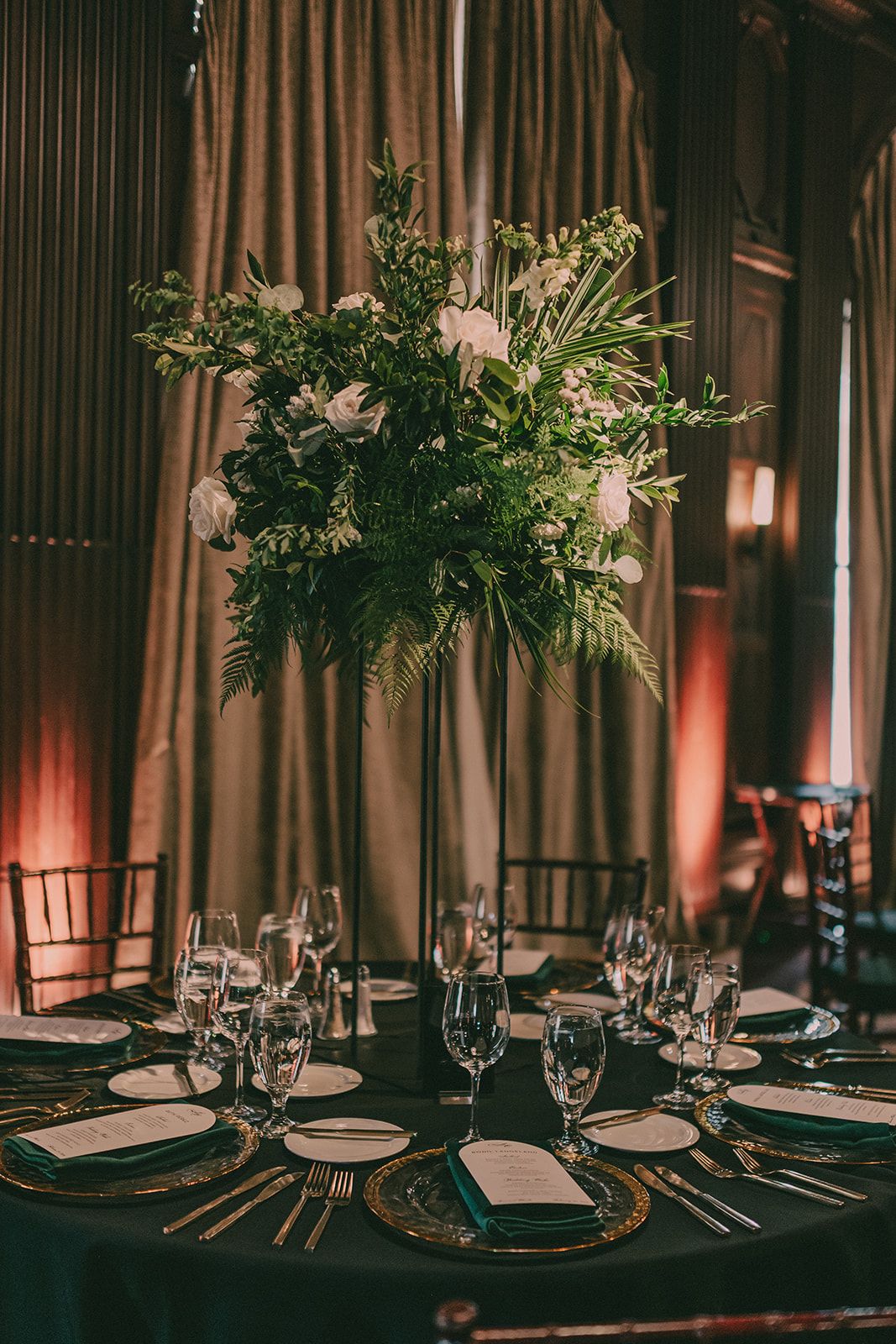 Tall green-and-white floral arrangement above a dark-green reception table.