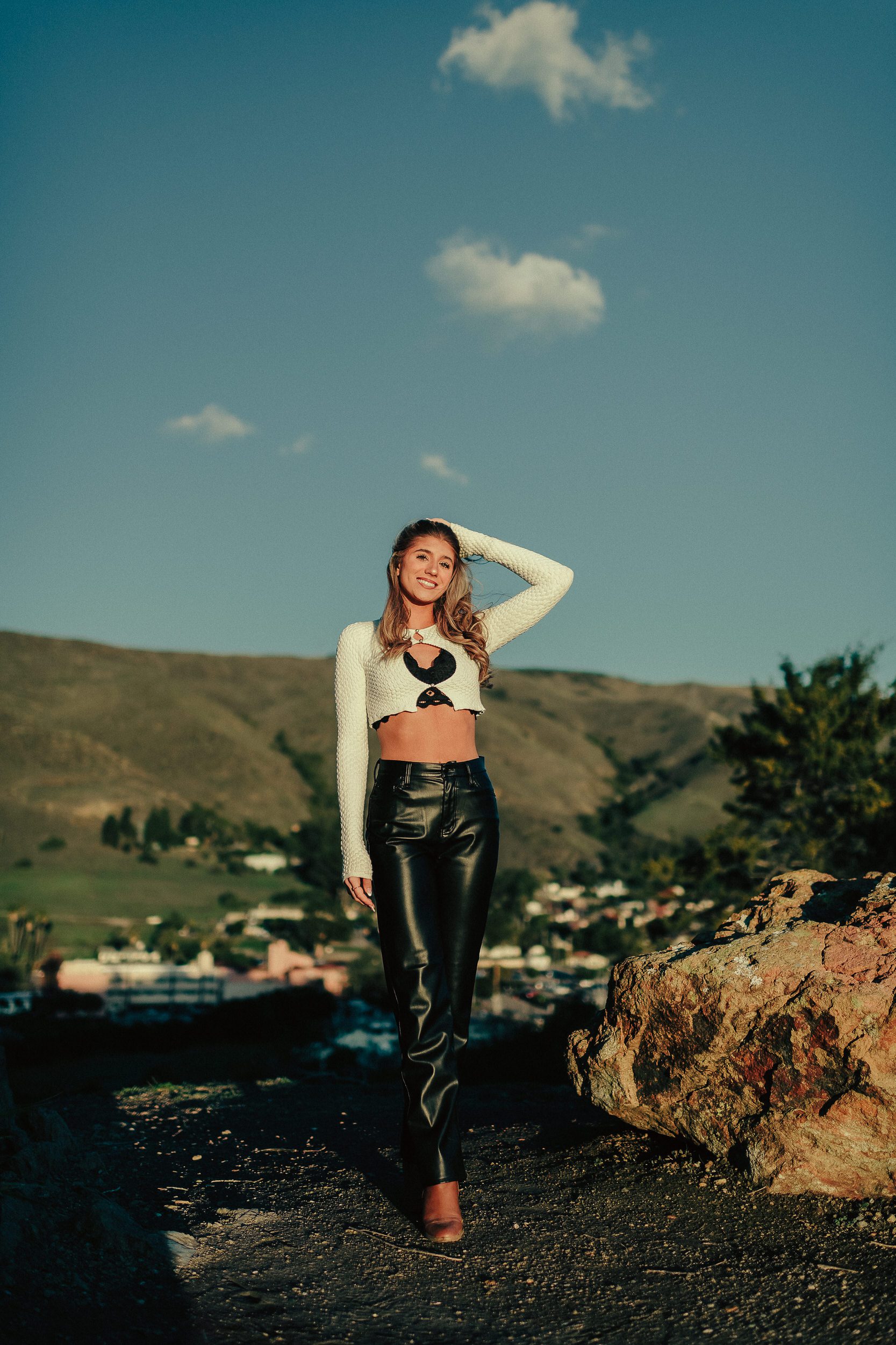 Full-length senior portrait on coastal rocks beneath a blue sky