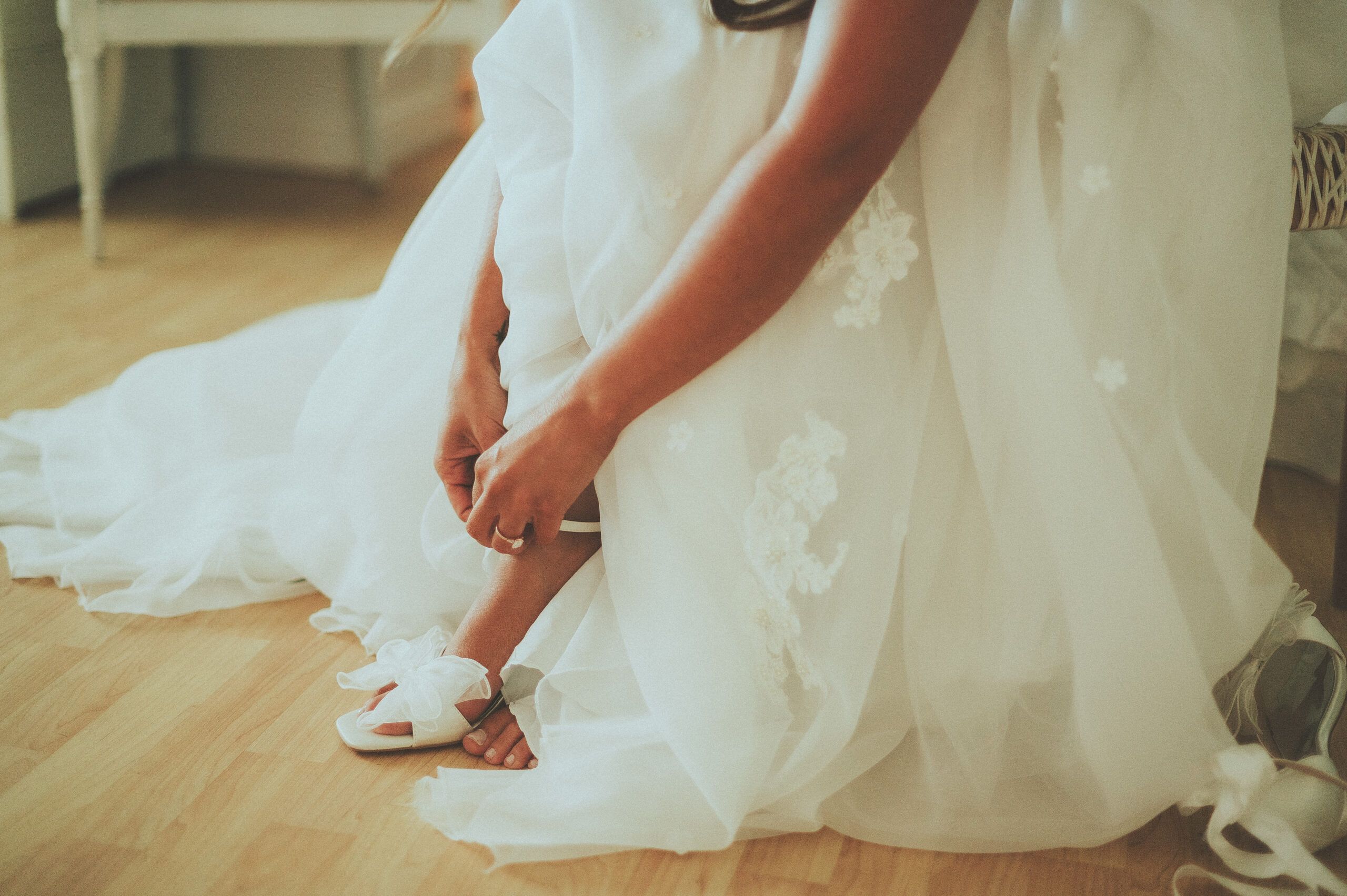 Hands fastening a wedding shoe beneath layers of lace and tulle.