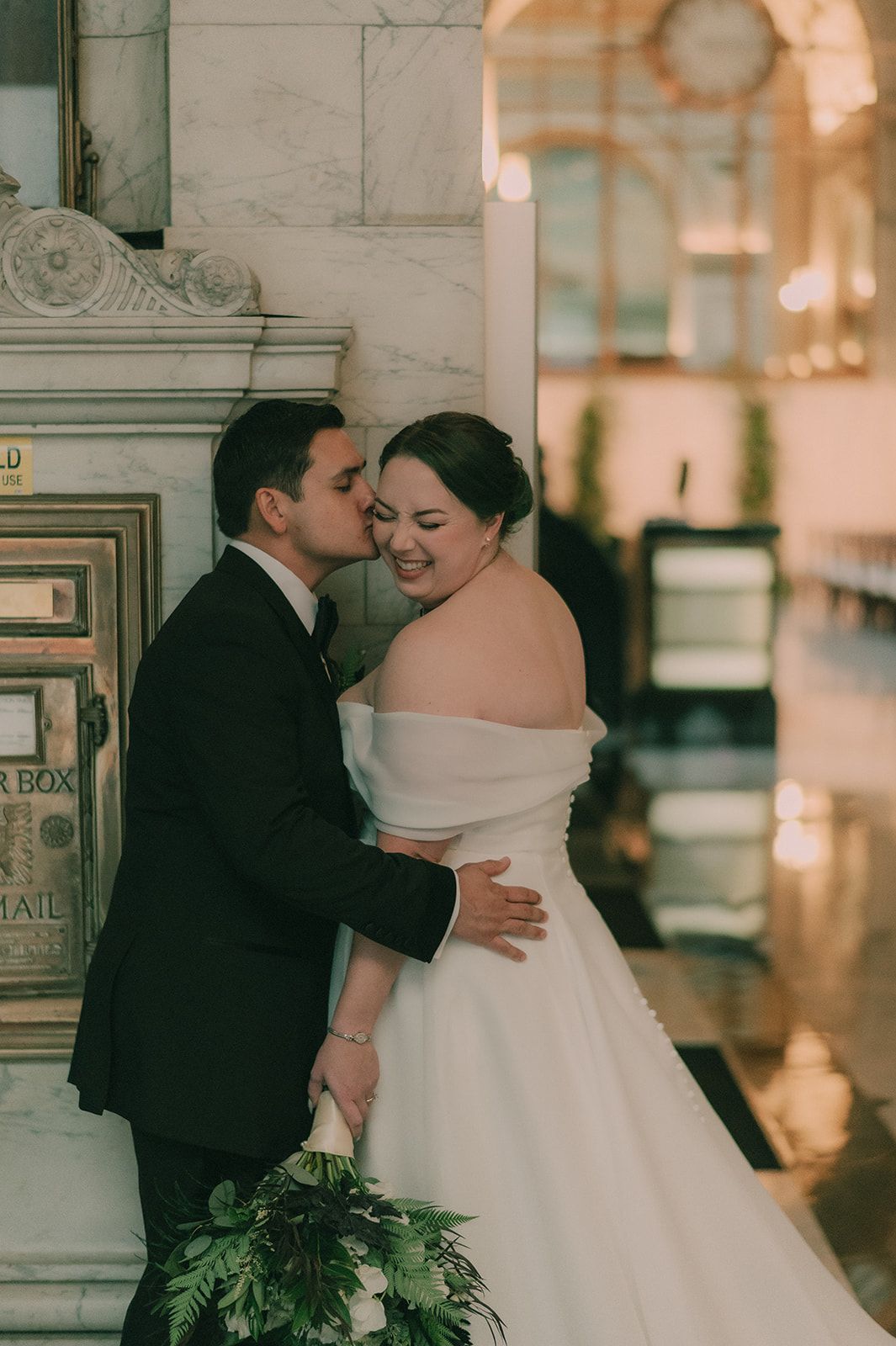 Charles kisses Anne's cheek as she laughs beside a vintage marble mail box.