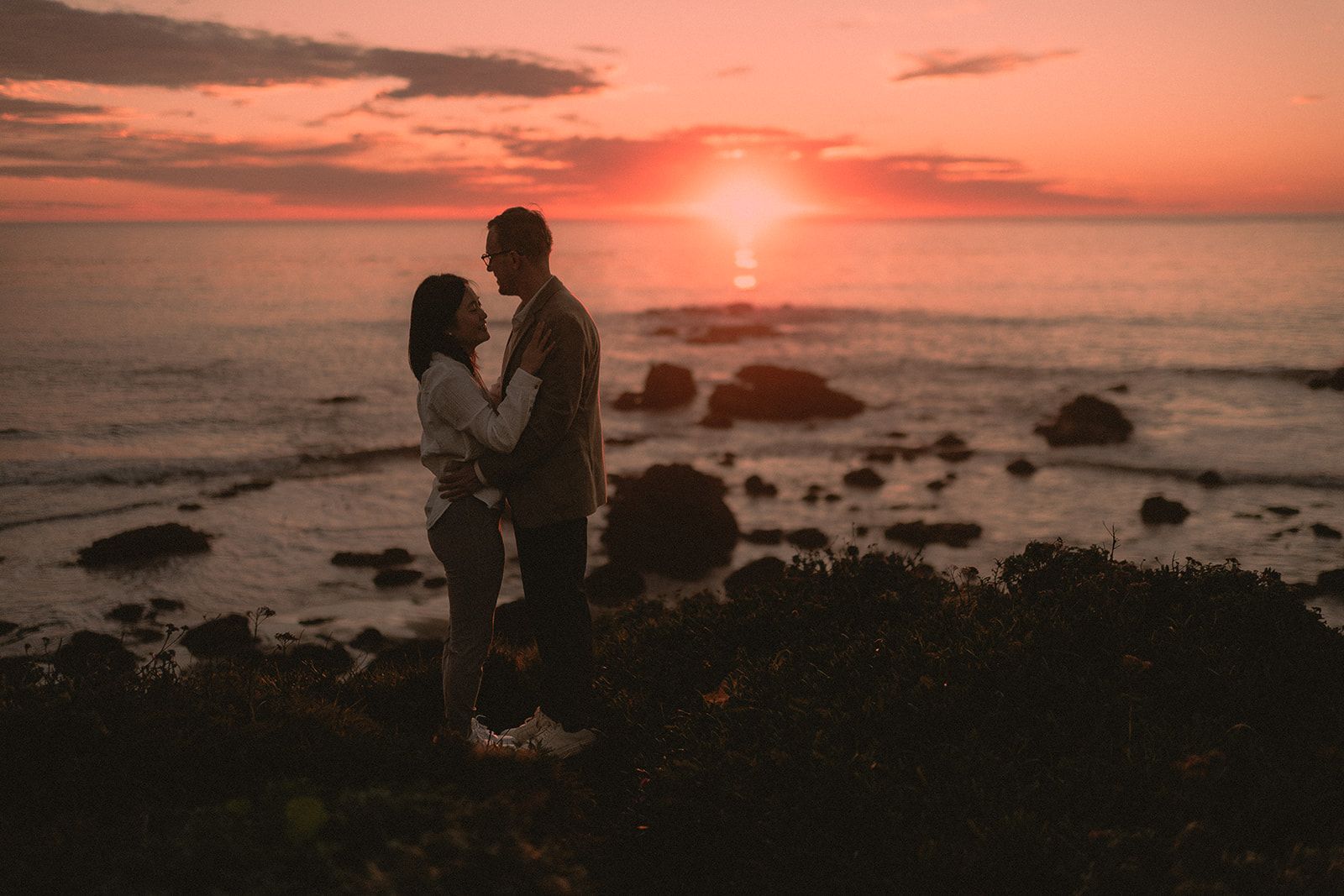 Couple silhouetted against a saturated ocean sunset after a proposal