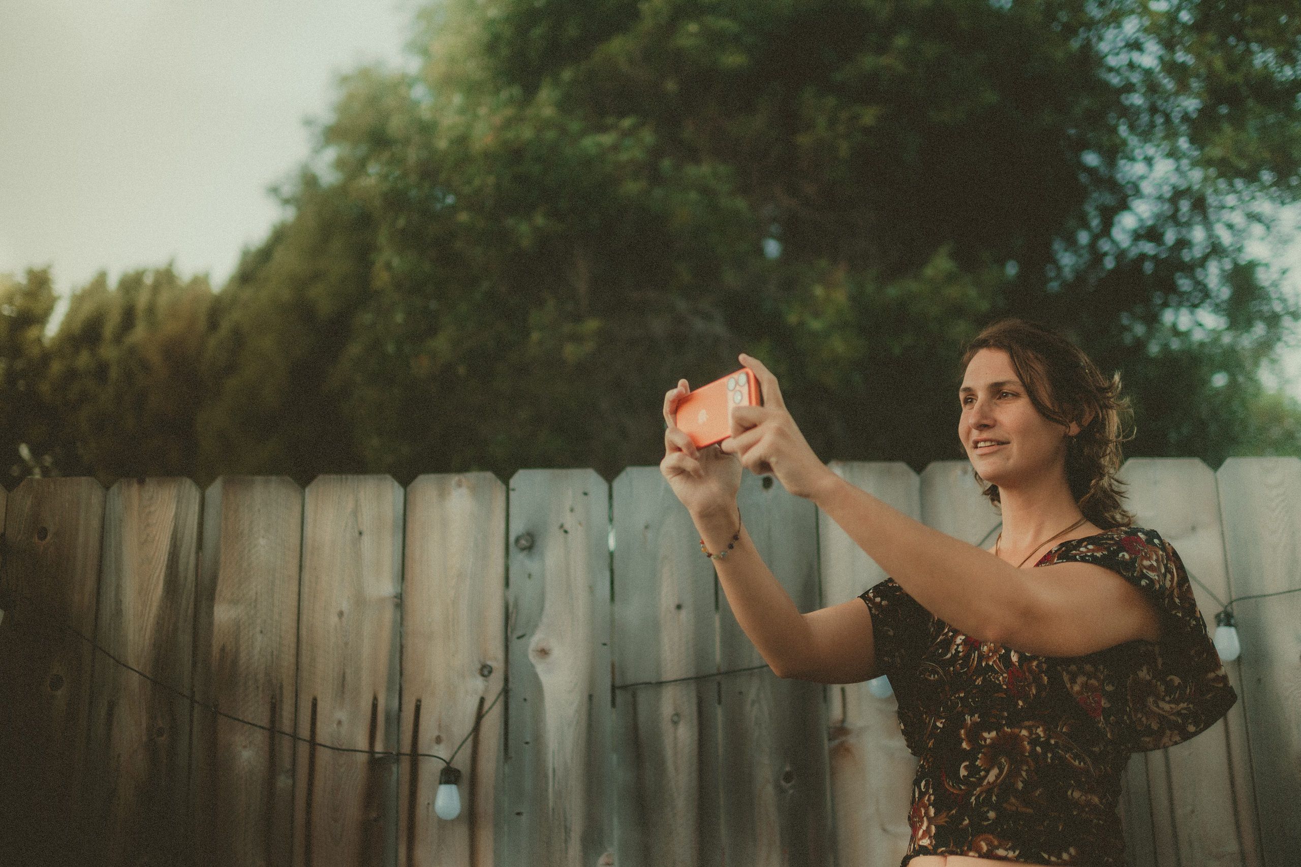 Faith filming with an iPhone beside a wooden fence.