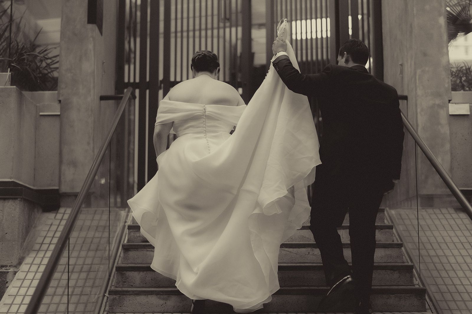 Black-and-white view of Anne and Charles walking up an outdoor staircase framed by tall city columns.