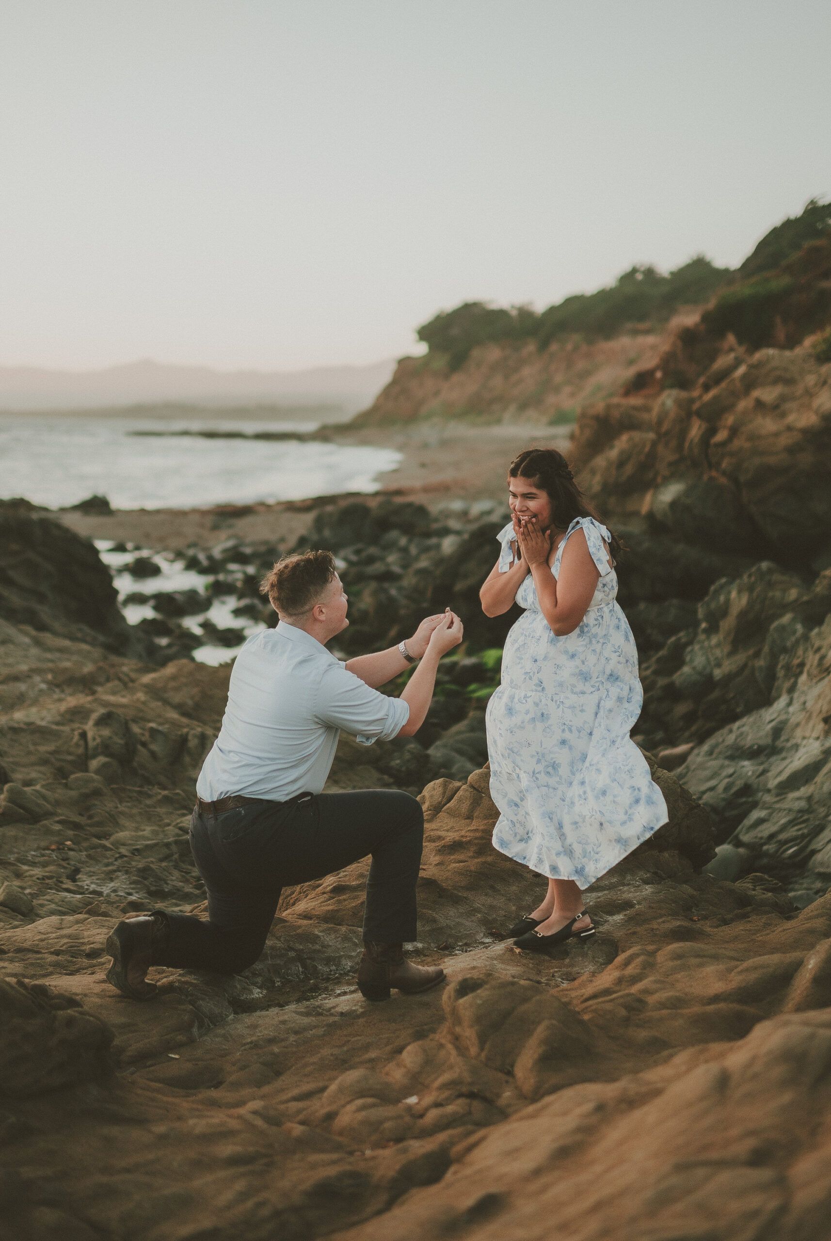 Alissa reacting with delight as Jaydon proposes on a rocky beach