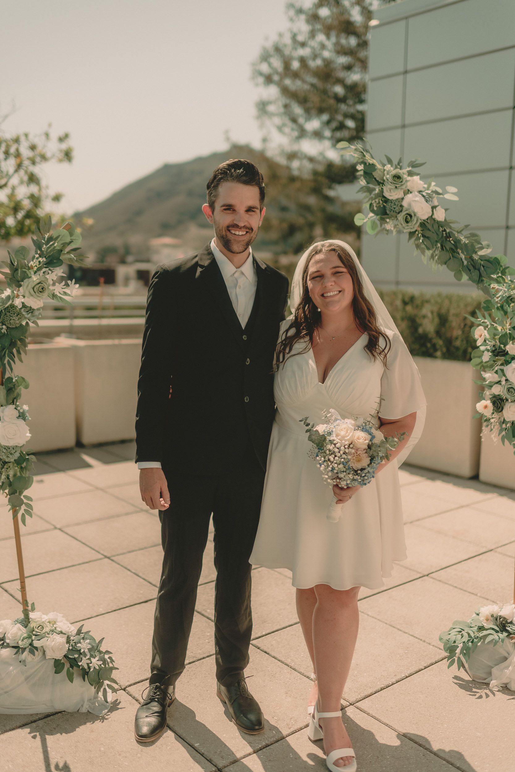 Tiffani and Braden stand beneath the floral arch with a wedding guest.