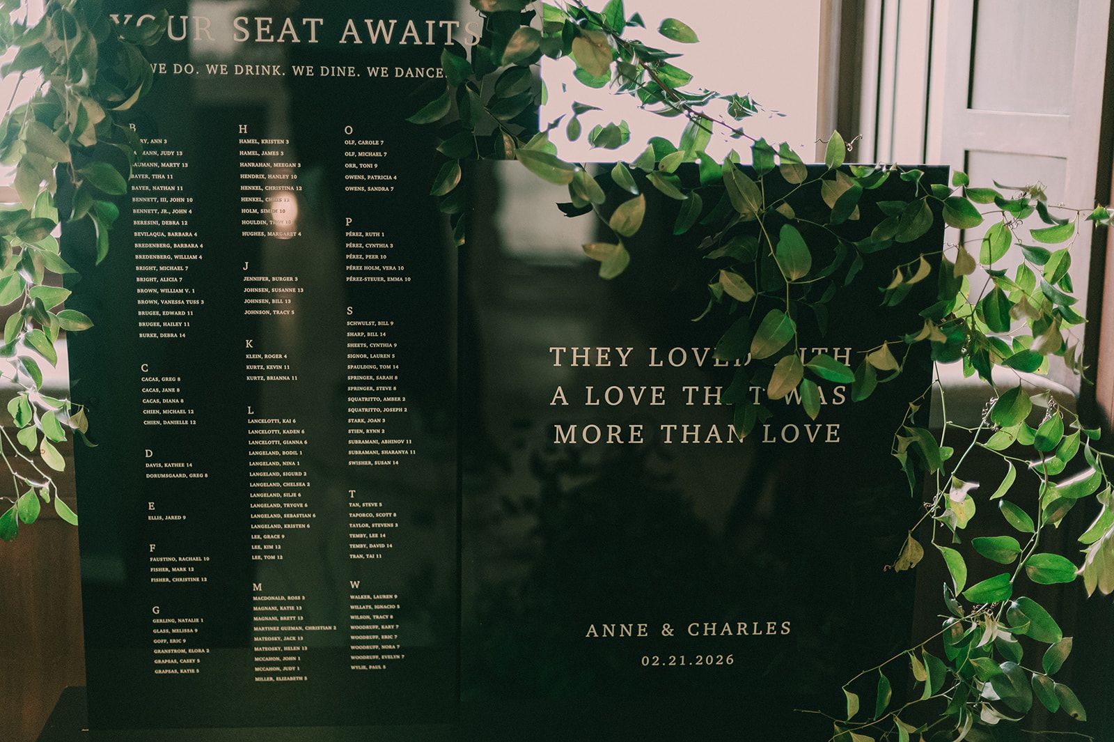 Deep-green wedding seating chart framed with trailing greenery and gold lettering.