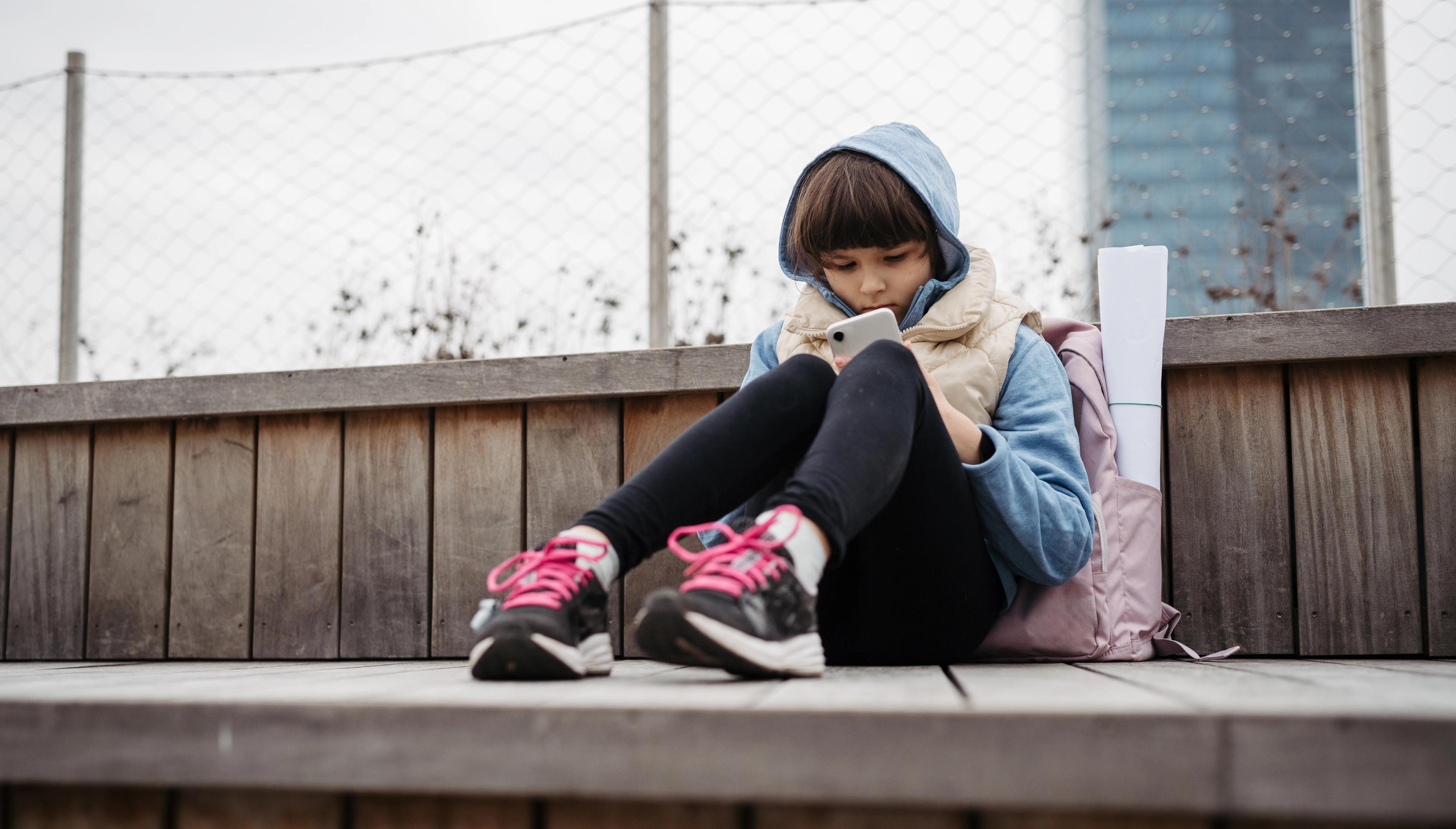 Skolepige sidder alene og ser på mobil