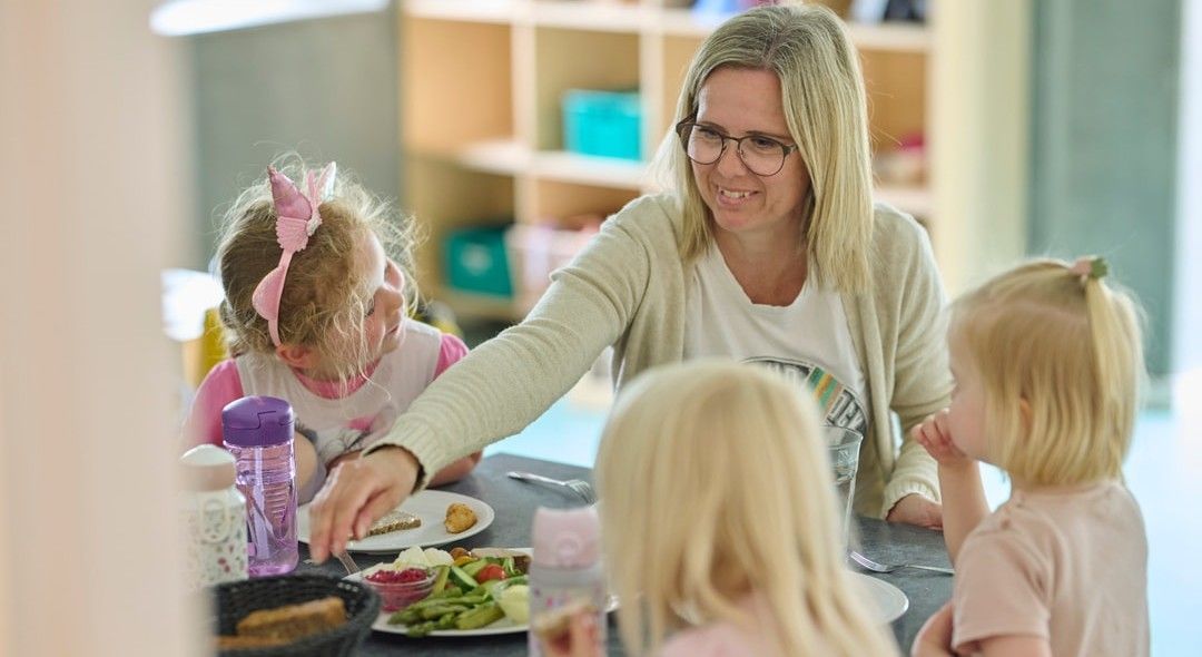 Pædagogisk assistent sidder med tre børnehavebørn omkring et bord