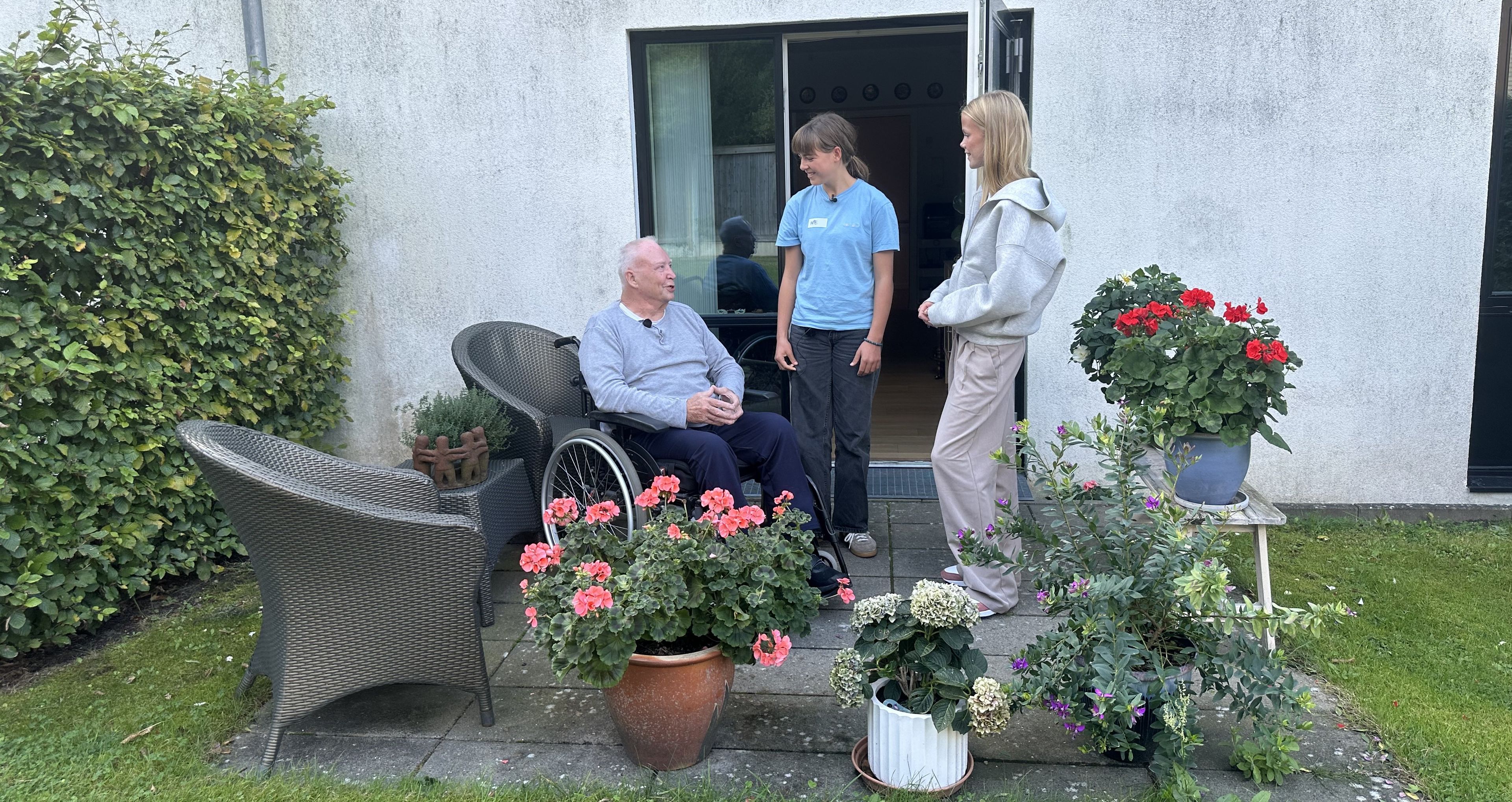 To elever i snak med pljehjemsbeboer i kørestol