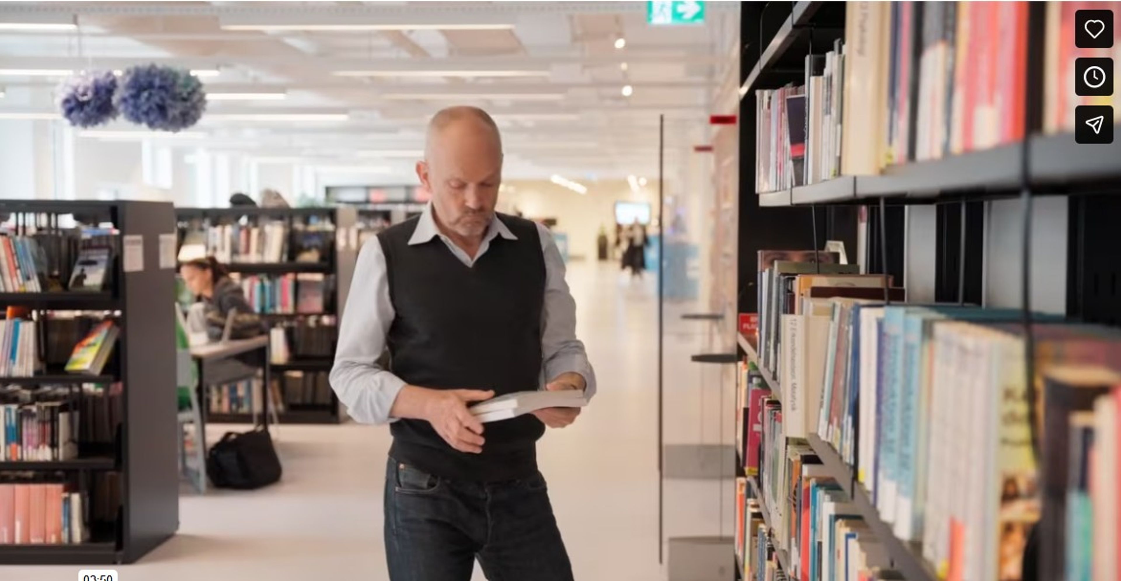 Studerende på uddannelse til pædagogisk assistent står foran bogreol og læser i en bog