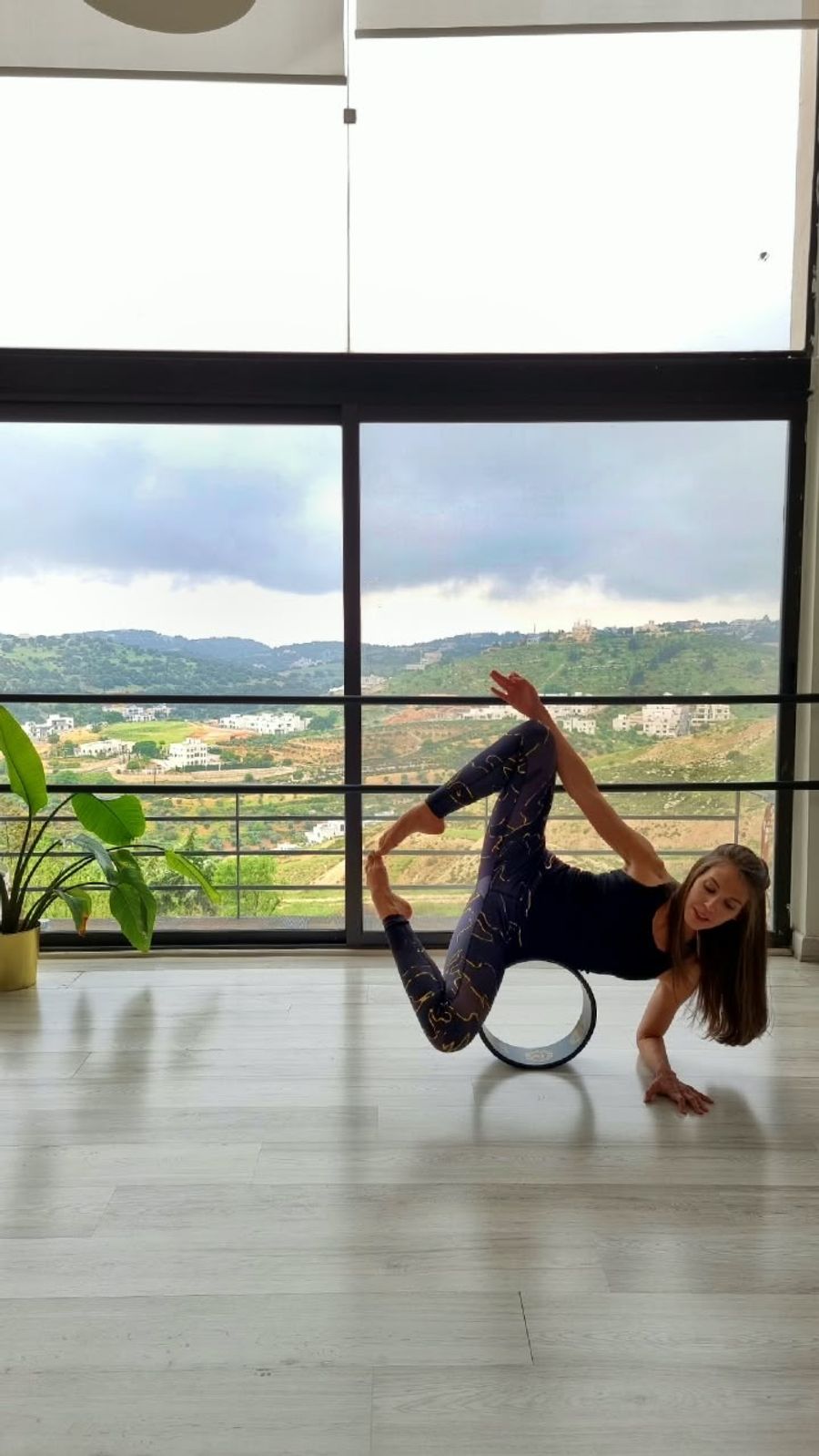 Deena balancing on a yoga wheel in a bright room, the hills of Amman through the window behind her.