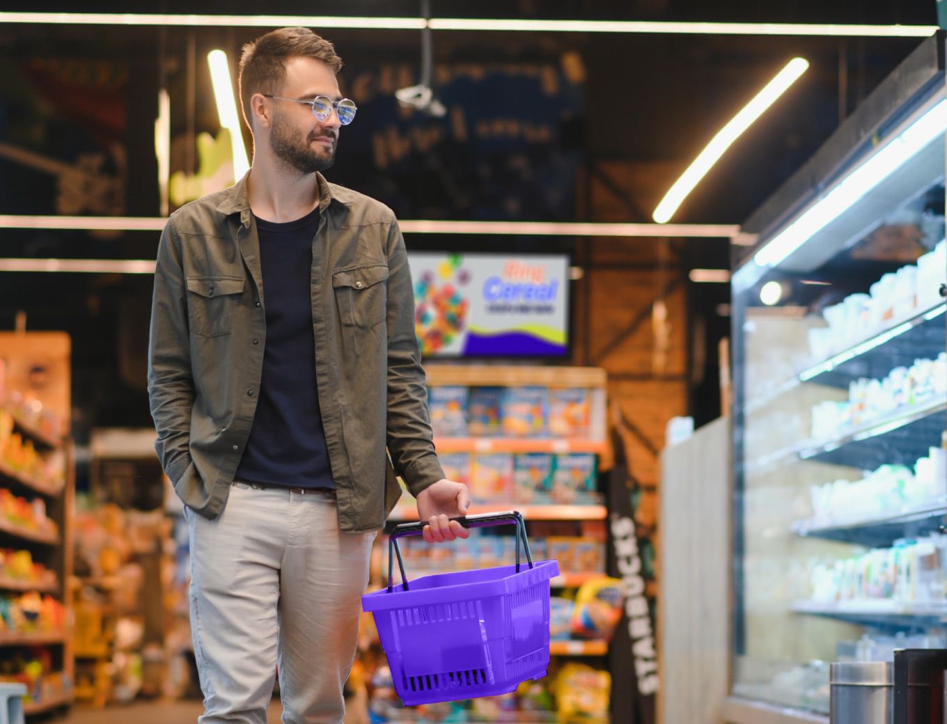 Man walking through grocery story holding a basket with retail media being displayed in the background