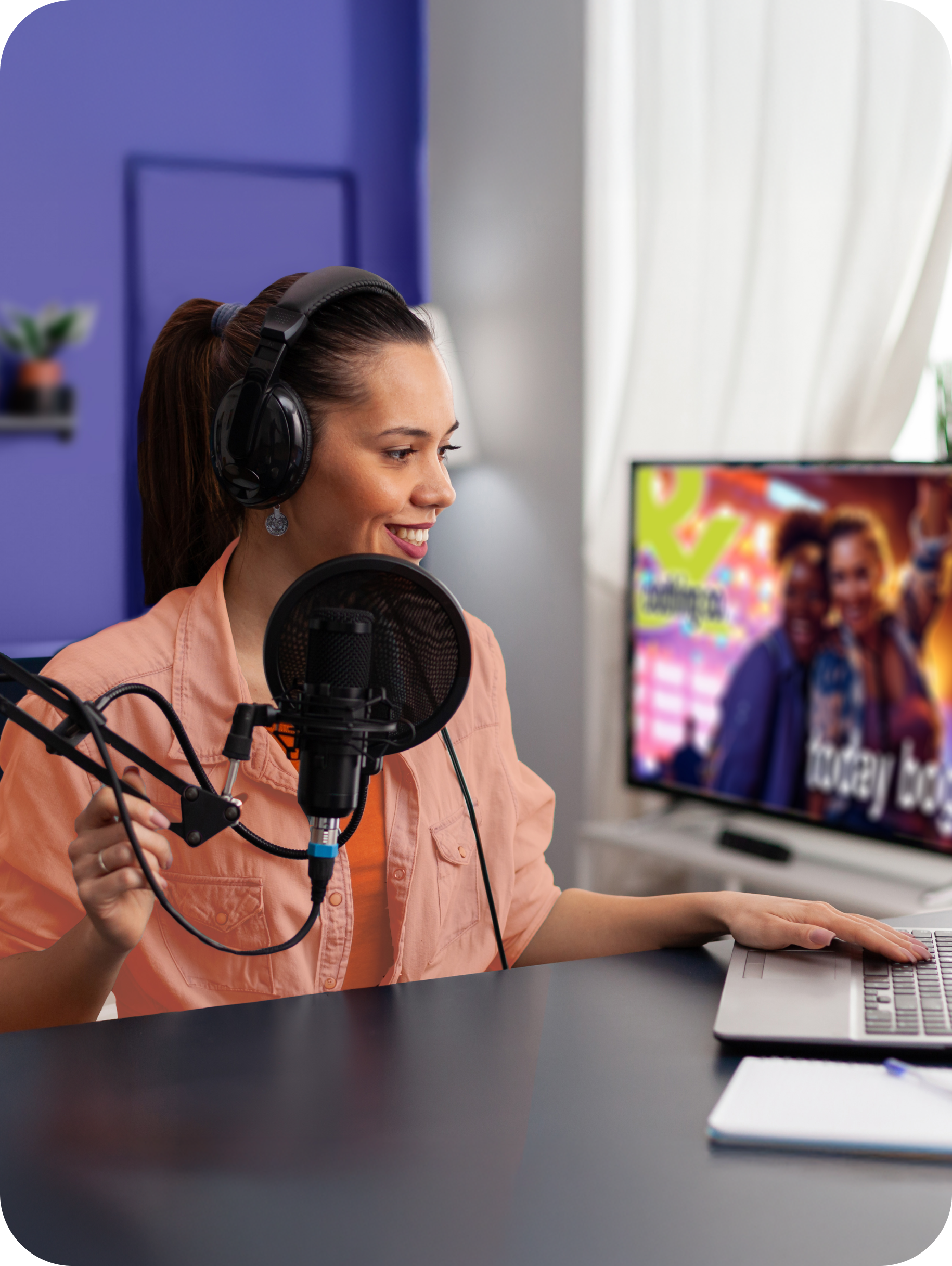 Image of a woman sitting at a desk talking into a mic and working on her computer