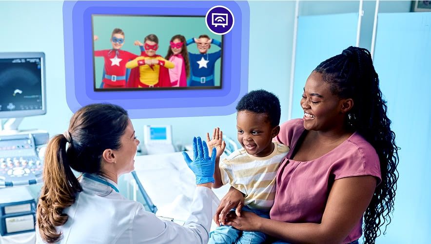 A child watching kid-friendly TV content during a pediatric medical visit while a clinician engages with the family.