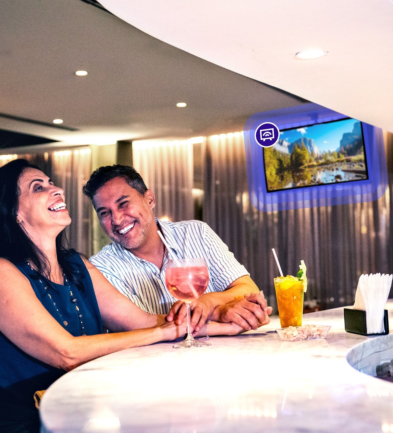 Hotel bar lounge with guests watching curated TV content on a wall-mounted screen