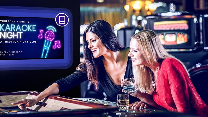 Two women gambling with Rockbot Digital Signage being displayed behind them