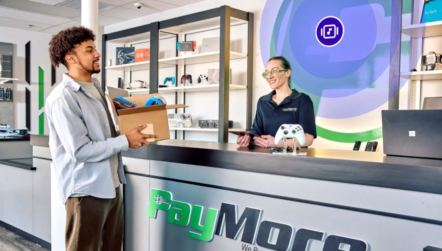 PayMore store employee and customer at the retail counter with electronics displays