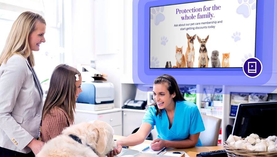 Healthcare staff assisting patients at a front desk with a digital screen displaying important information and services.