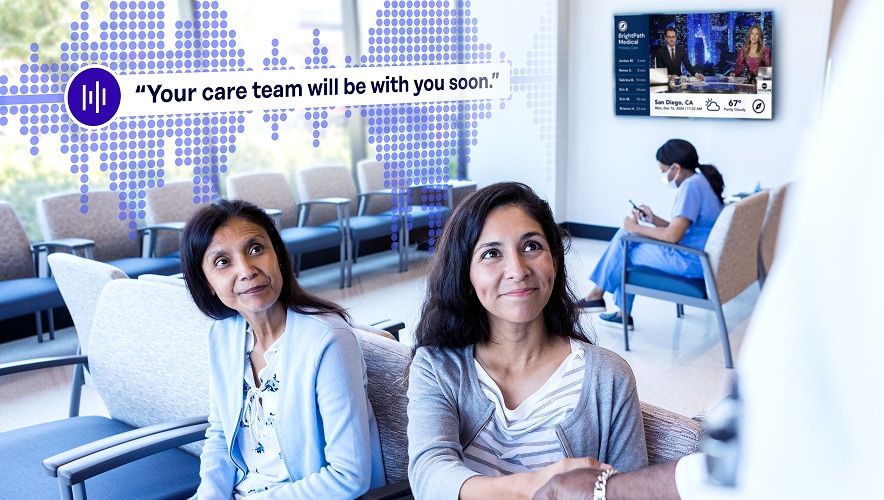Patients in a healthcare waiting room with an audio message displayed, indicating the care team will be with them soon.