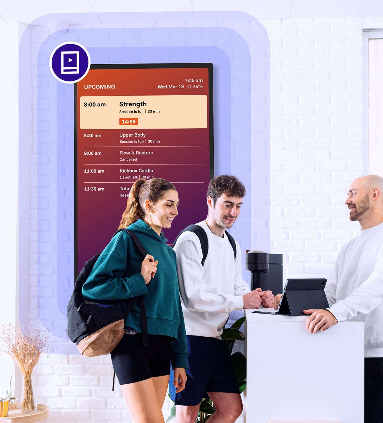 Fitness studio members checking digital class schedule signage at front desk