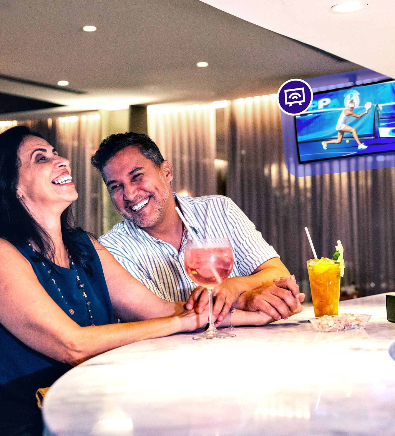 Hotel bar lounge with guests watching curated TV content on a wall-mounted screen