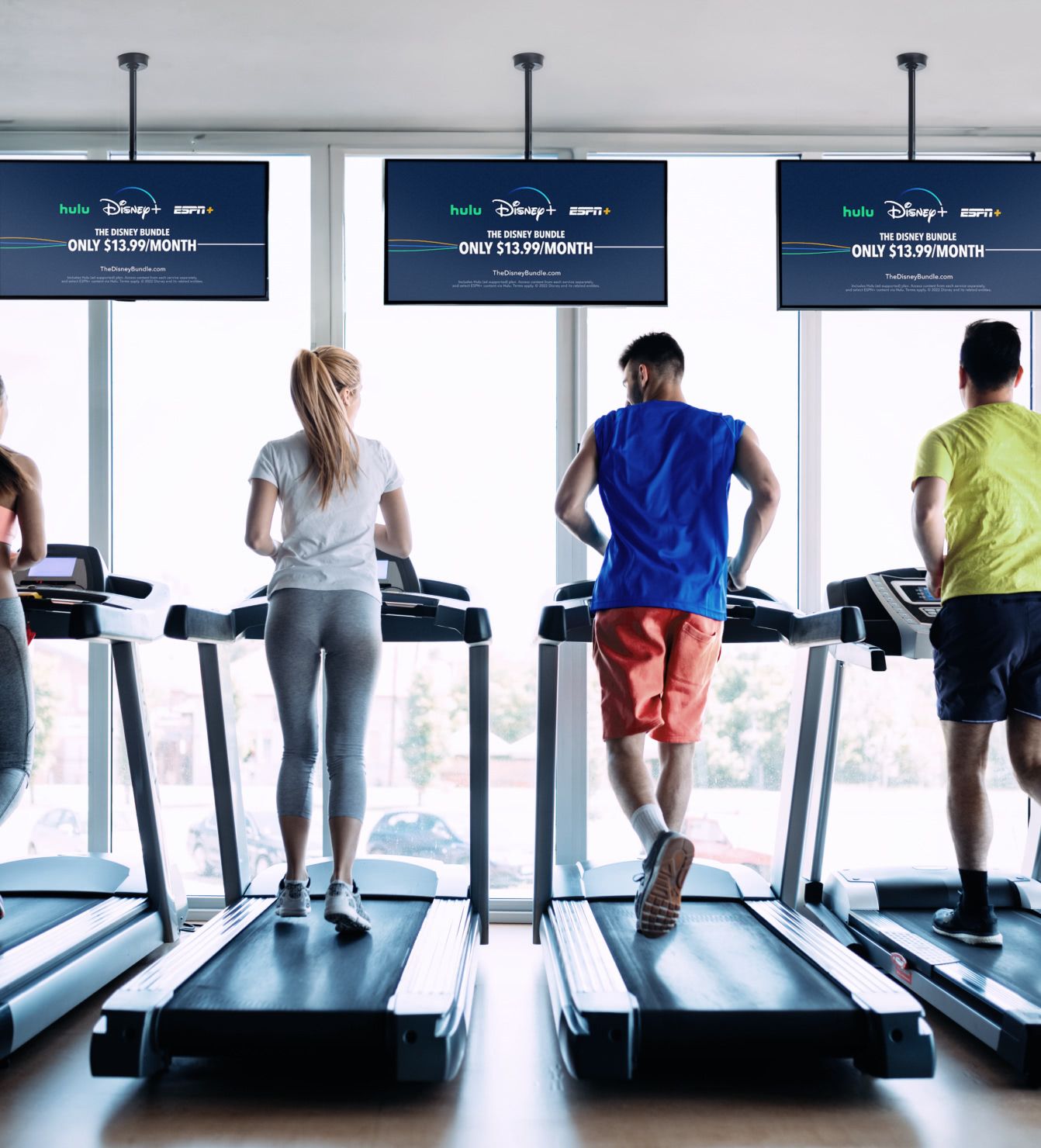 Gym members running on treadmills while TV screens with Rockbot advertising play in front of them.