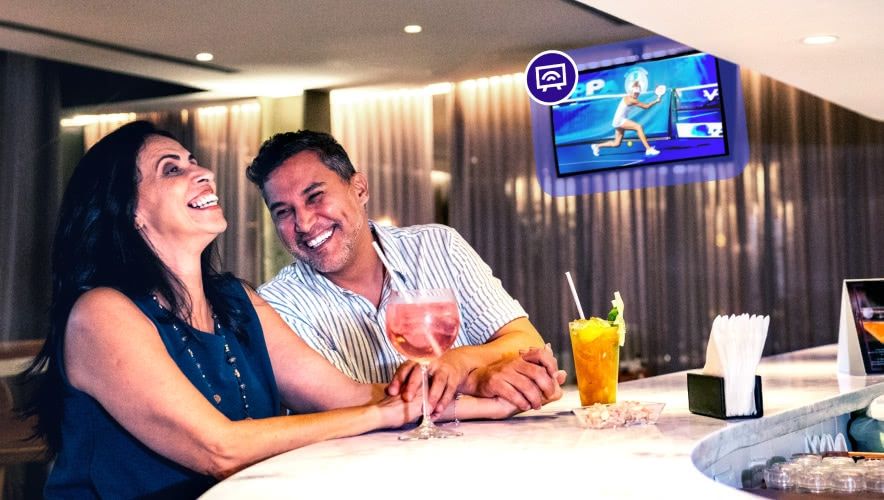 Hotel bar lounge with guests watching curated TV content on a wall-mounted screen