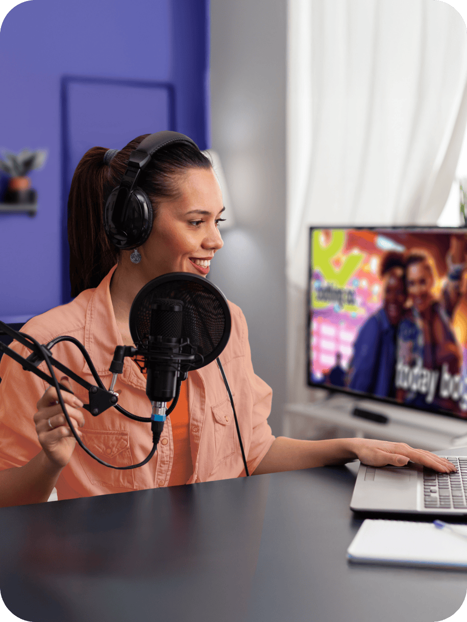 Image of a woman sitting at a desk talking into a mic and working on her computer