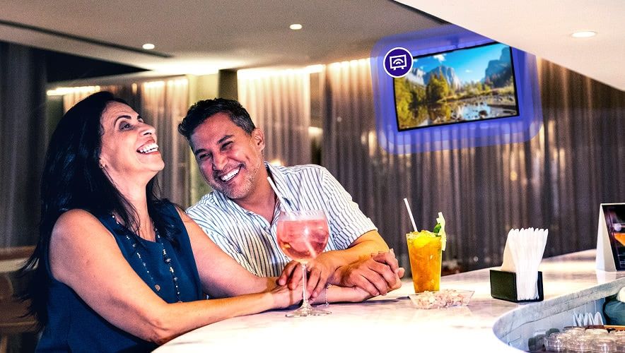Hotel bar lounge with guests watching curated TV content on a wall-mounted screen