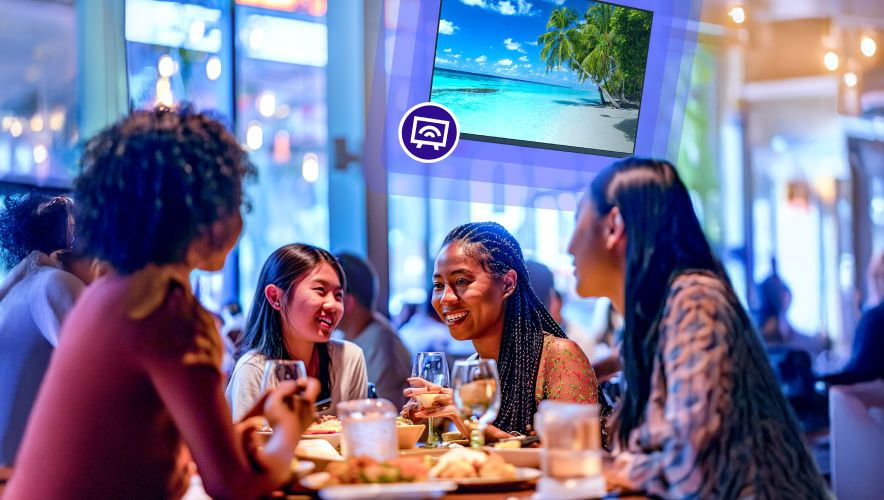 People sitting around a table eating with Rockbot TV playing behind them