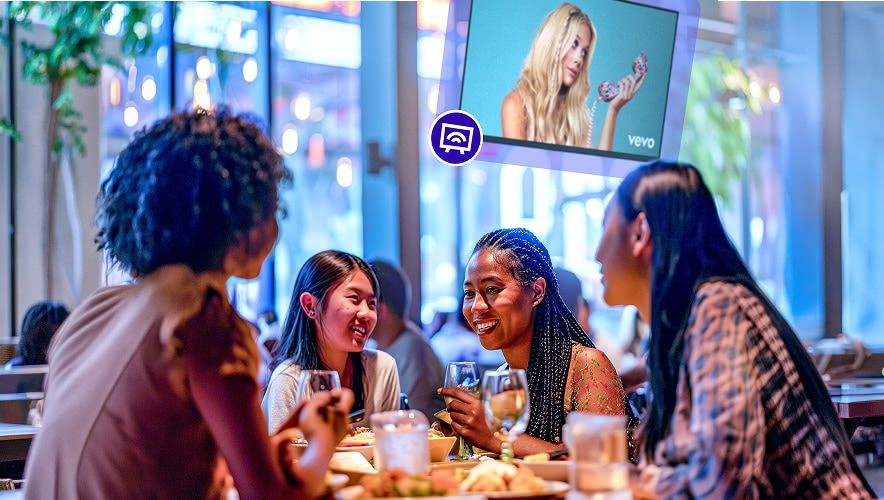 People sitting around a table eating with Rockbot TV playing behind them