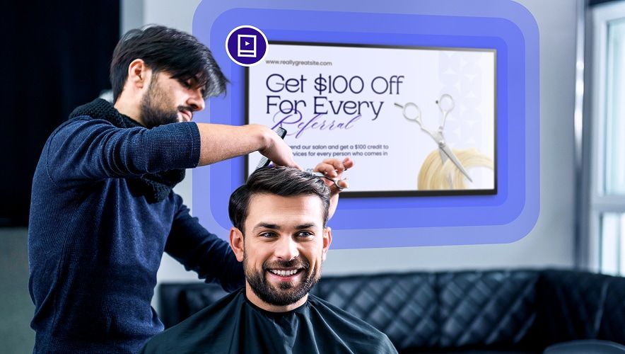 Stylist cutting a client’s hair with digital signage promoting salon services