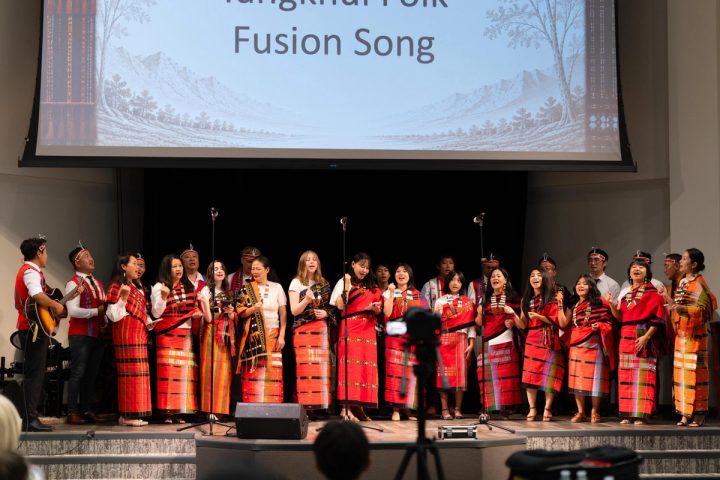 Photograph of a large ensemble standing on stage beneath a Fusion Song slide at the First Naga Baptist Fundraising Cultural Event.