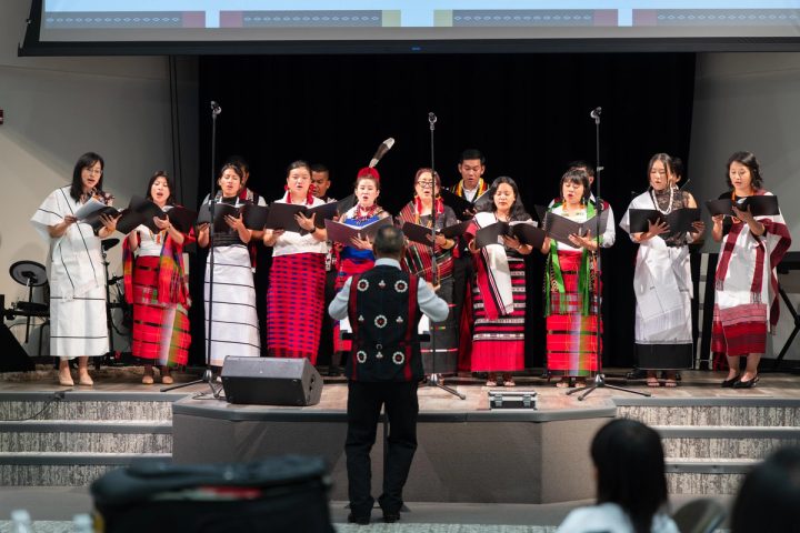 Photograph of a large group of performers in traditional attire gathered on stage at the First Naga Baptist Fundraising Cultural Event.