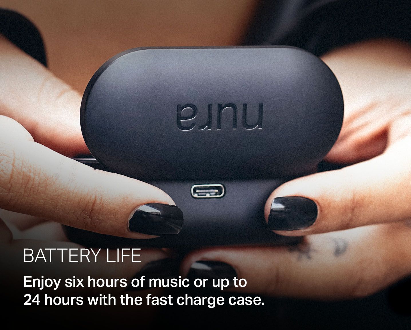 Close-up shot of hands holding the NURATRUE earbuds battery case, with overlay text: "Battery life. Enjoy six hours of music or up to 24 hours with the fast charge case."