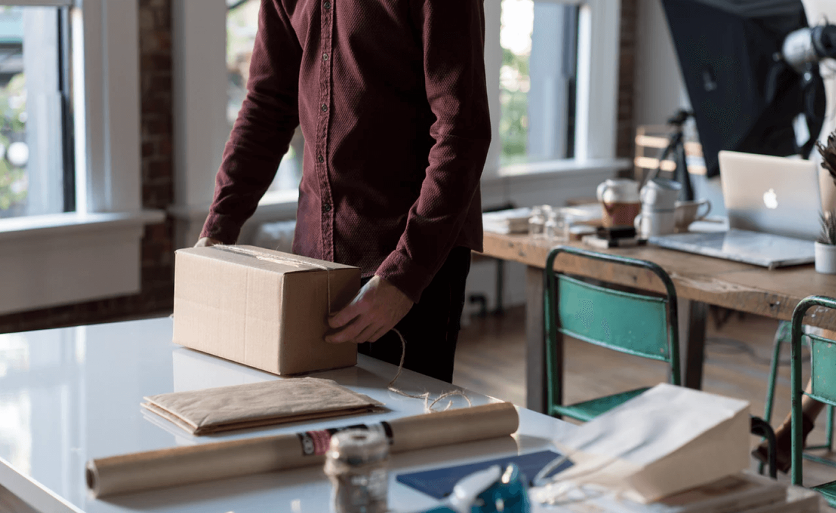 A man packing a cardboard parcel for delivery in a studio workspace