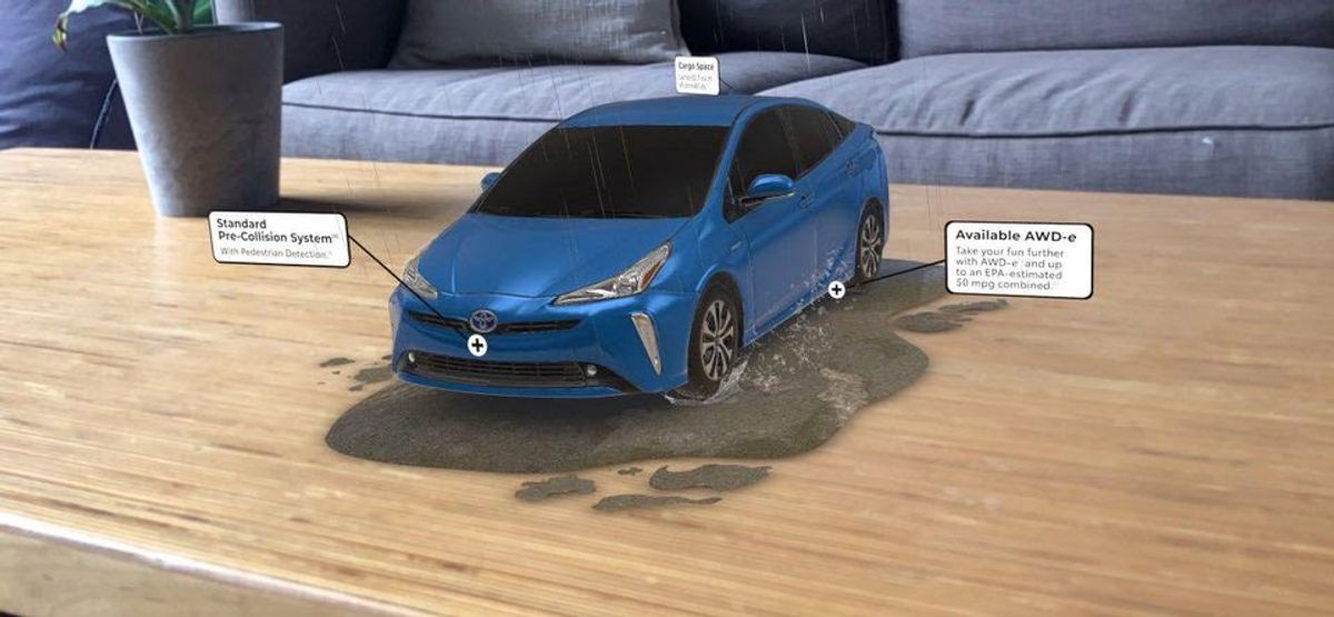 A blue Toyota Prius rendered in augmented reality on a living-room coffee table, driving through a puddle, with callouts for its standard pre-collision system and available AWD-e