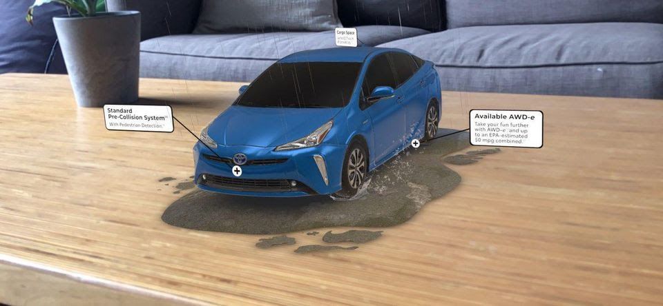 A blue Toyota Prius rendered in augmented reality on a living-room coffee table, driving through a puddle, with callouts for its standard pre-collision system and available AWD-e