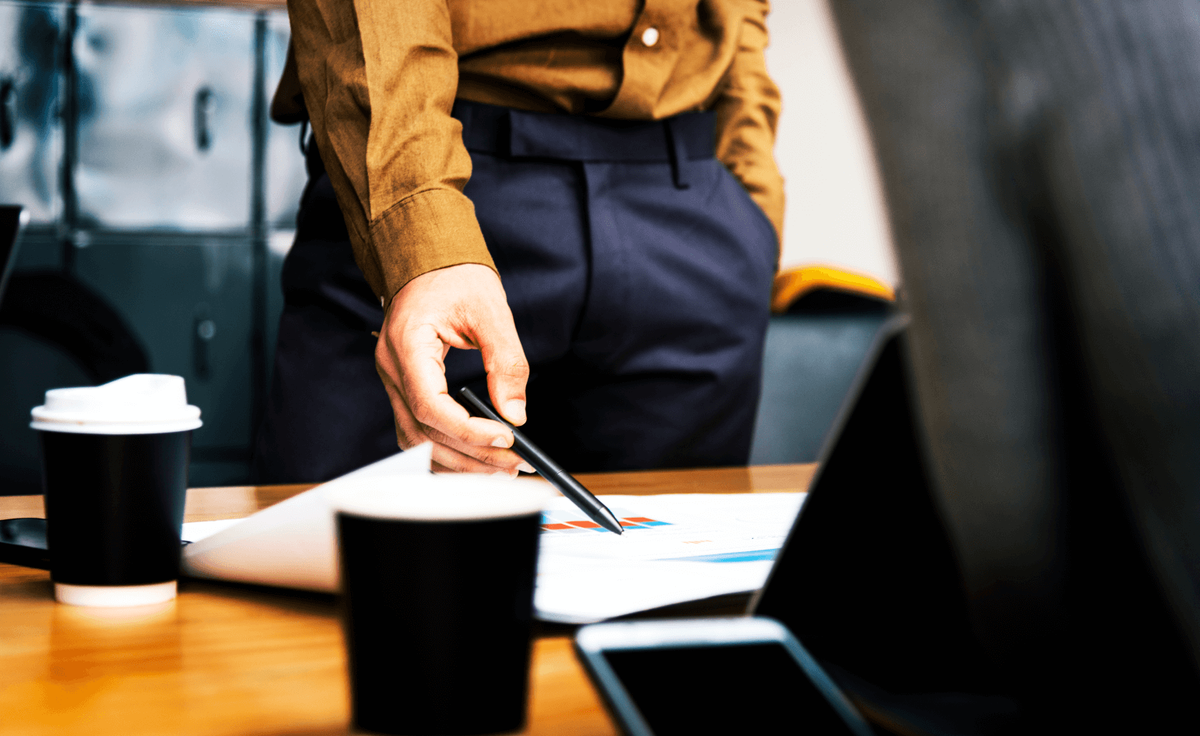 A salesperson pointing a pen at a printed sales chart on a desk