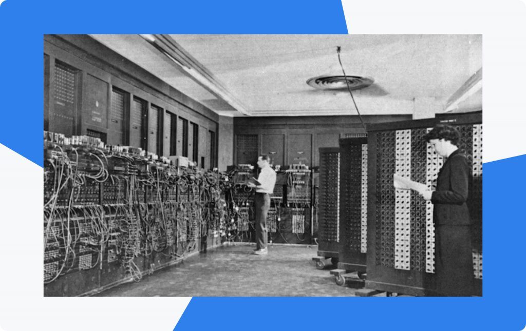Archive photograph of the ENIAC room, two operators setting switches on wall-sized racks of early computing hardware