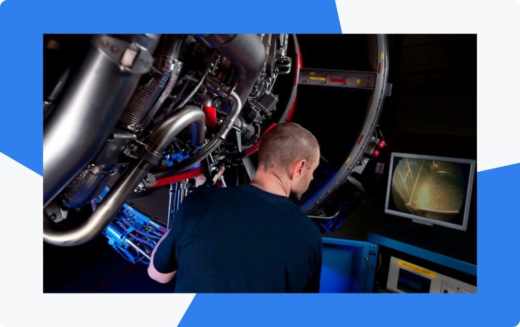 An engineer inspecting a jet engine with a borescope, the probe's internal view shown on a monitor beside him