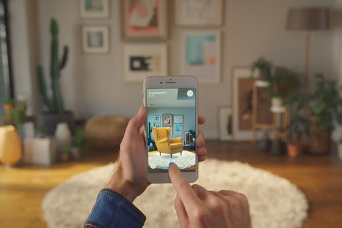 Someone holding a phone up to a living room, the IKEA app placing a yellow armchair on the rug through the camera view