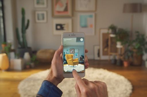 Someone holding a phone up to a living room, the IKEA app placing a yellow armchair on the rug through the camera view