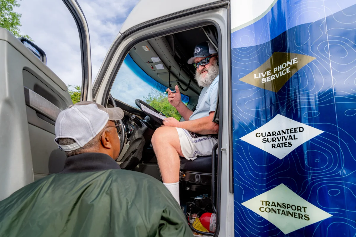 A man discussing his pond with a truck driver from Arkansas Pondstockers who is sitting in a semi truck.