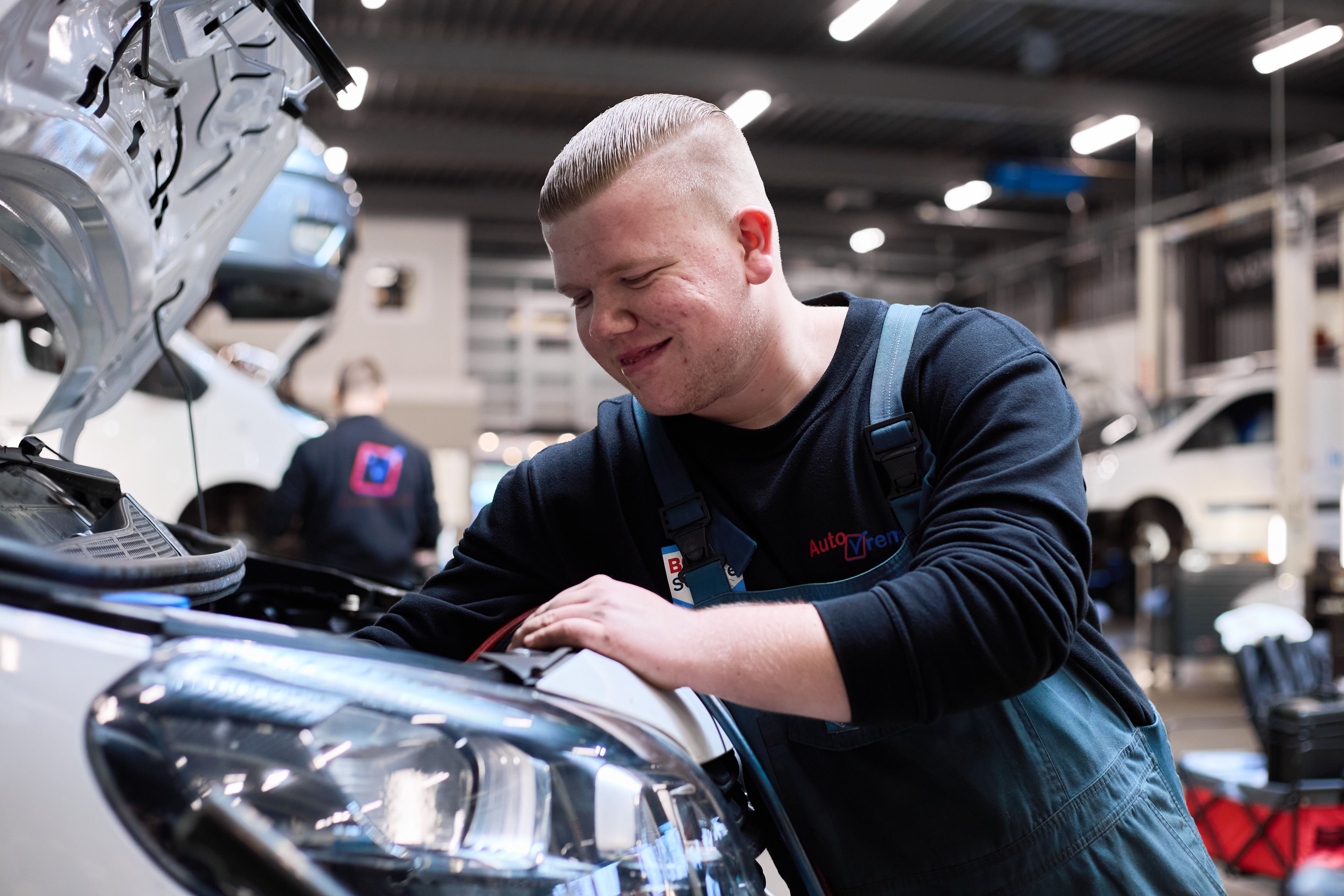Lachende monteur in overall werkt onder de motorkap van een auto.